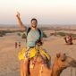 Tourist riding camel across golden sand dunes at sunset