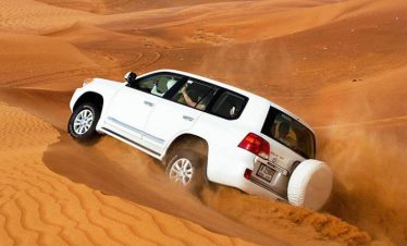desert safari experience in Sharjah with tourists riding 4x4 vehicles over golden sand dunes