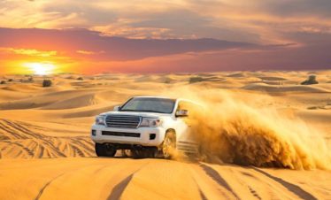 Golden desert dunes with SUV driving uphill.